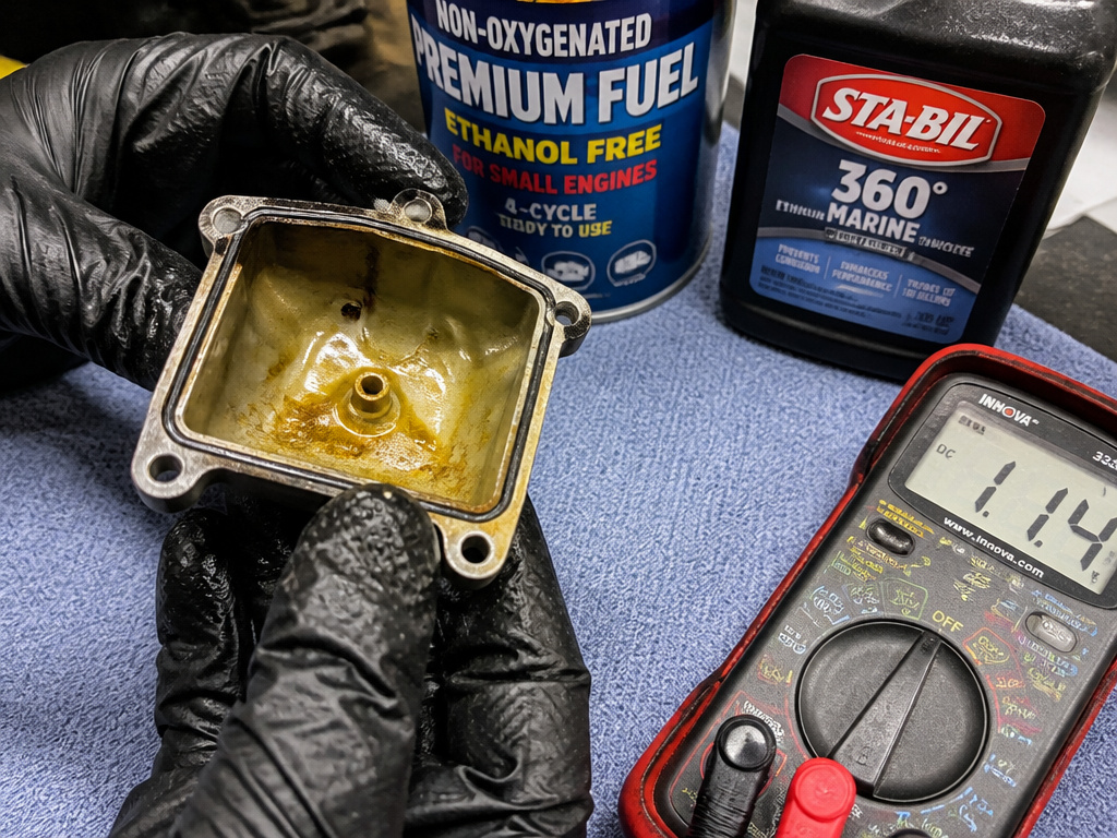 Carburetor bowl with yellow gunk and a multimeter showing low battery voltage.