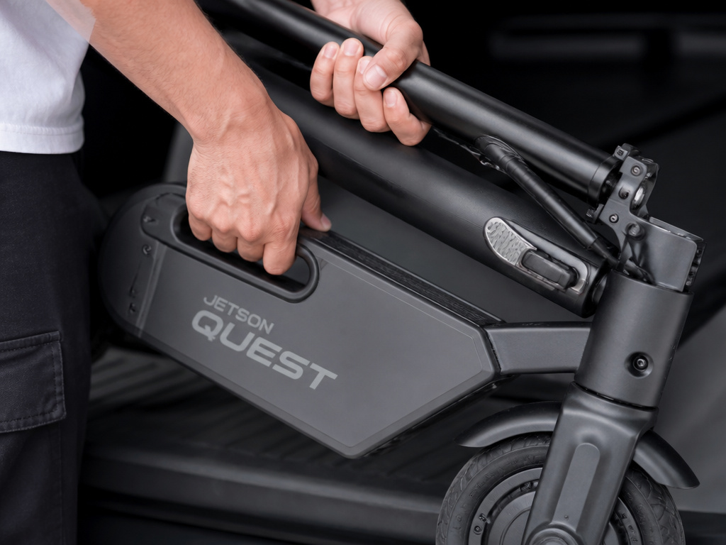 Close-up of hands carrying a folded Jetson Quest electric scooter.