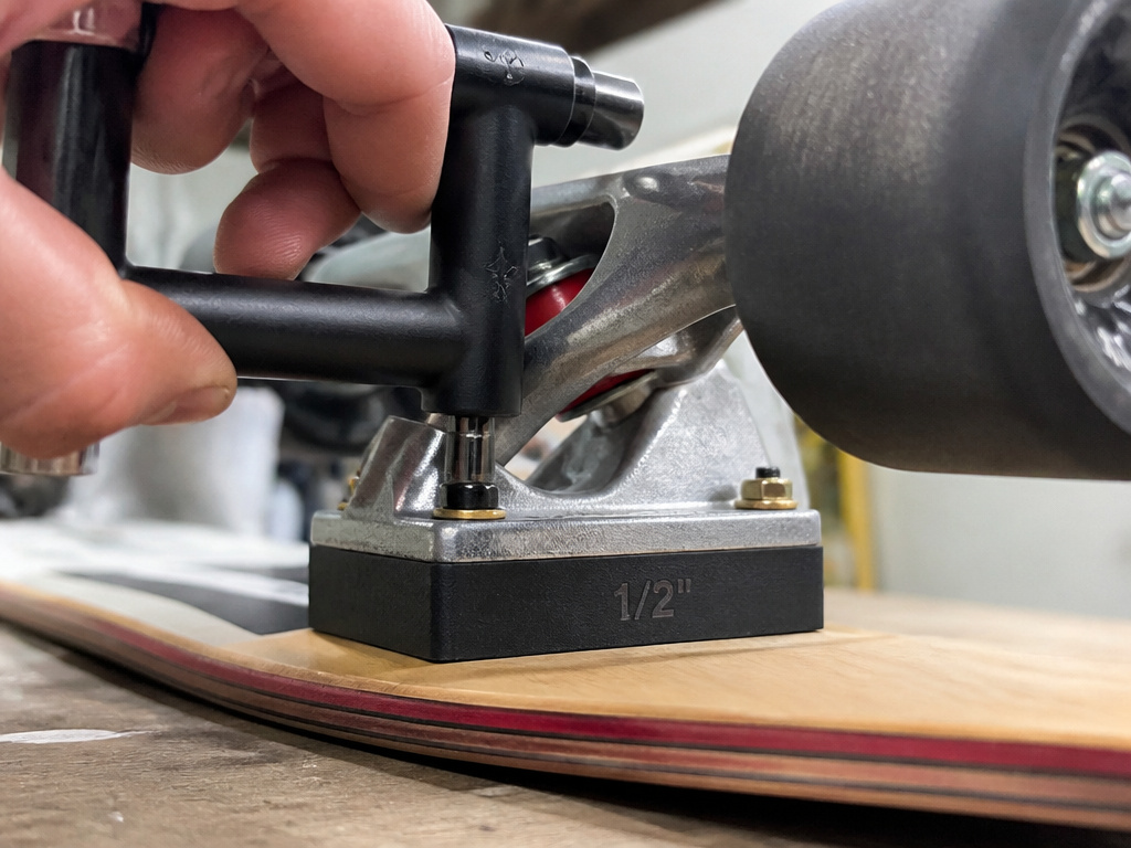 Installing a hard plastic riser pad on a longboard truck to prevent wheel bite.
