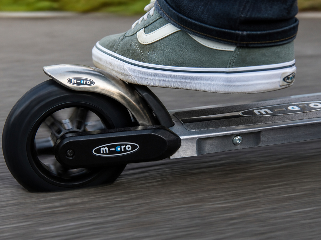 Close-up of a micro scooter's rear foot brake being engaged by a rider.