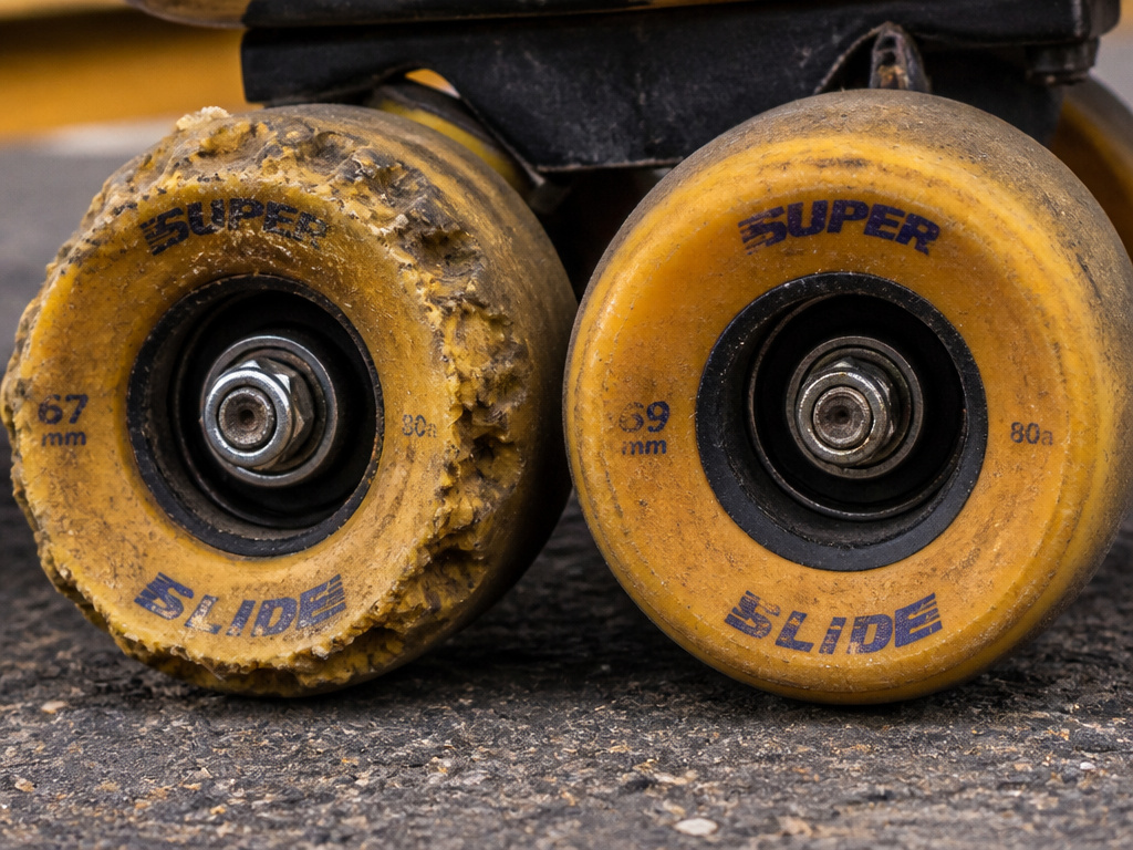 Close-up comparison of worn versus mildly worn longboard wheels on pavement.