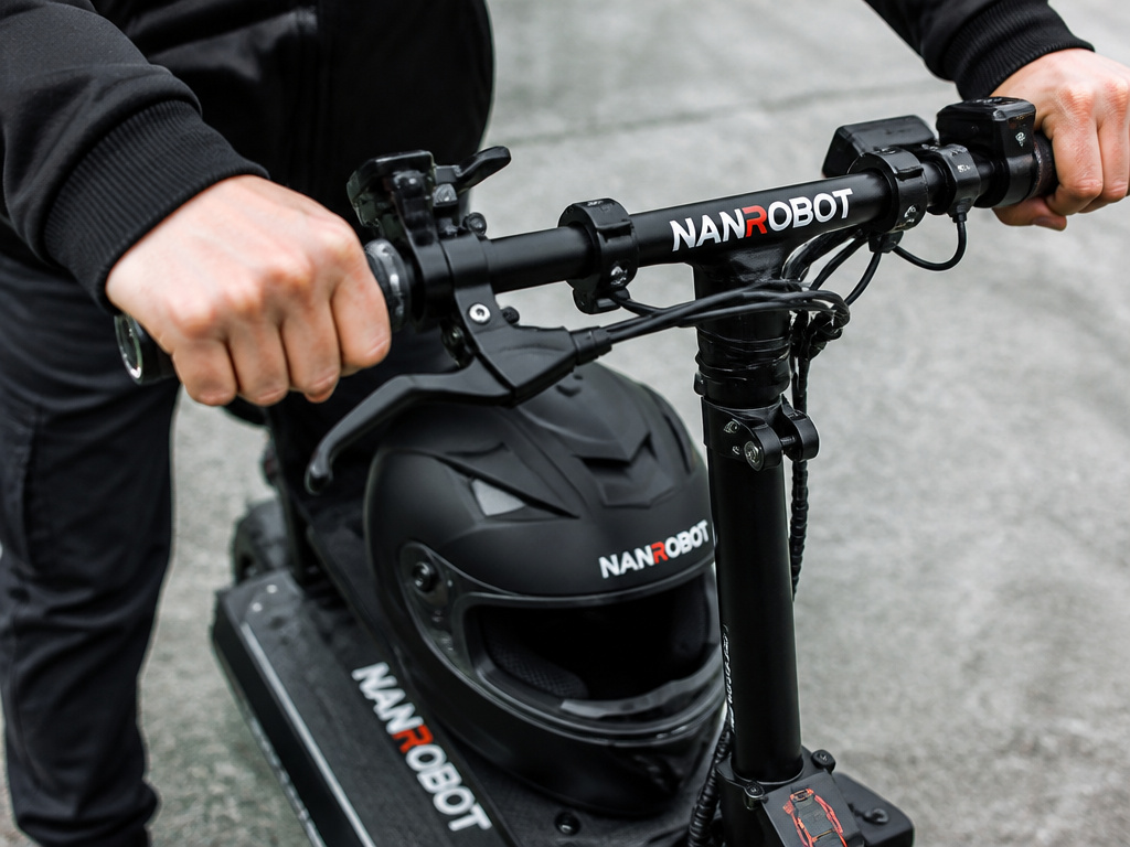 Close-up of hands on Nanrobot scooter controls with a full-face safety helmet.